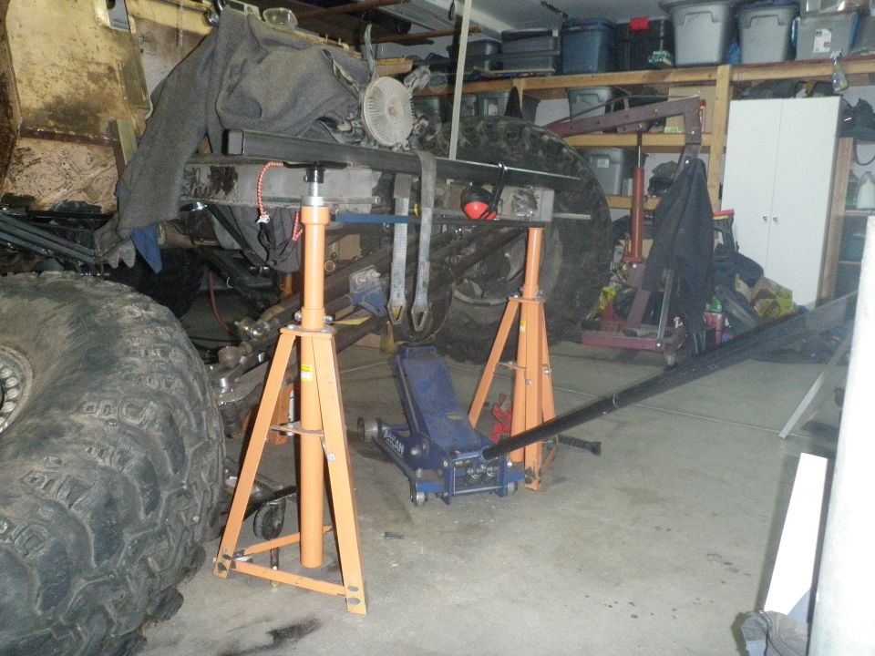 Vehicle chassis supported by orange jack stands and a blue floor jack in a garage