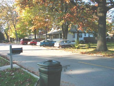 1997 Ford Taurus - Autumn residential street scene with a row of cars parked along the far curb, including a silver sedan, a dark blue sedan and a red pickup,…