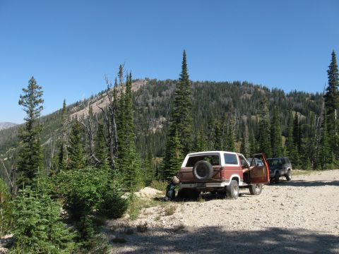 1981 Ford Bronco - Two SUVs are parked on a dirt road with a hill and trees in the background.