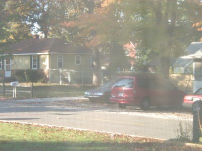 1997 Ford Taurus - Hazy backlit view across a residential street where a red sedan is parked at the curb with a dark sedan just ahead of it and another red ca…