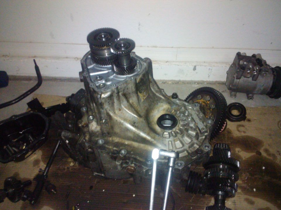 Disassembled transmission with gears visible, next to an air conditioning compressor