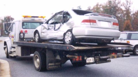 1989 Ford Bronco - A heavily damaged sedan is loaded onto a tow truck, with another vehicle visible in the background.