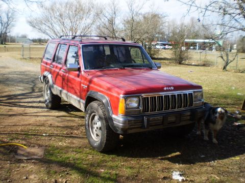 1992 Jeep Cherokee - A red 1992 Jeep Cherokee is seen parked in a yard with a dog standing next to it.