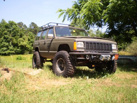 1992 Jeep Cherokee - Modified 1992 Jeep Cherokee with large tires and a roof rack sits in a field.
