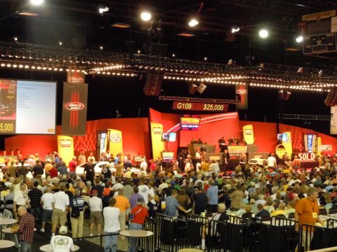 1982 Chevrolet Camaro - A large audience watches as a car is auctioned off on stage under bright lights.