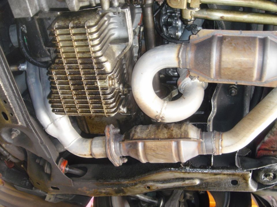 Underside dual catalytic converters and mandrel-bent downpipes beside a finned cooler