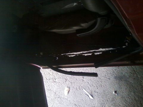 1988 Ford F-150 - The underside of a vehicle reveals significant rust and damage, with a black hose lying on the ground.
