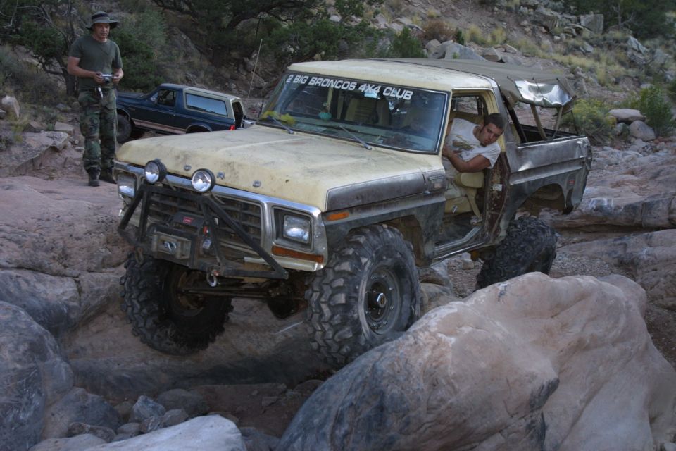 Tan open-top Ford Bronco rock crawling on off-road trail with driver inside