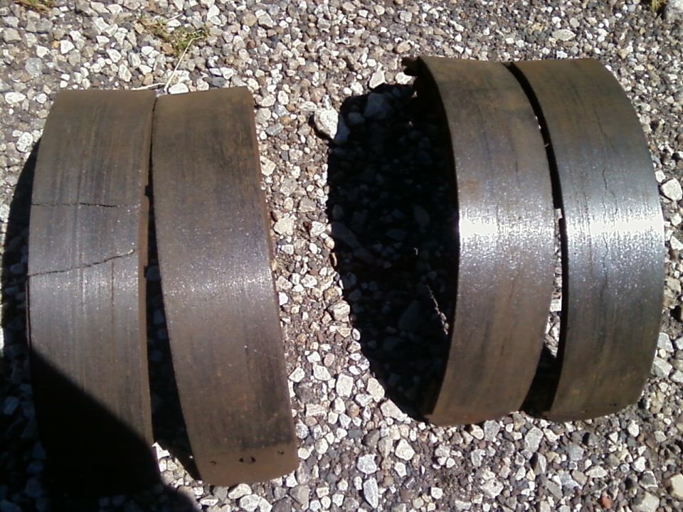 Two old, rusty brake drums sitting on gravel. One drum is cracked