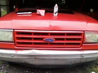 1988 Ford F-150 - The grille and headlights of a red pickup truck are visible. The hood is open, showing items on top.