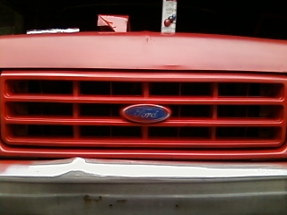 1988 Ford F-150 - Close-up of the front grille of a red Ford F-150, showing the iconic Ford emblem.