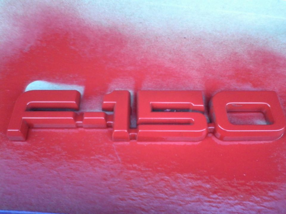 Red F-150 emblem on a red surface with white overspray