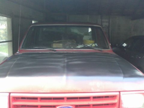 1988 Ford F-150 - Front view of a red truck with an unpainted hood, parked indoors next to another vehicle.