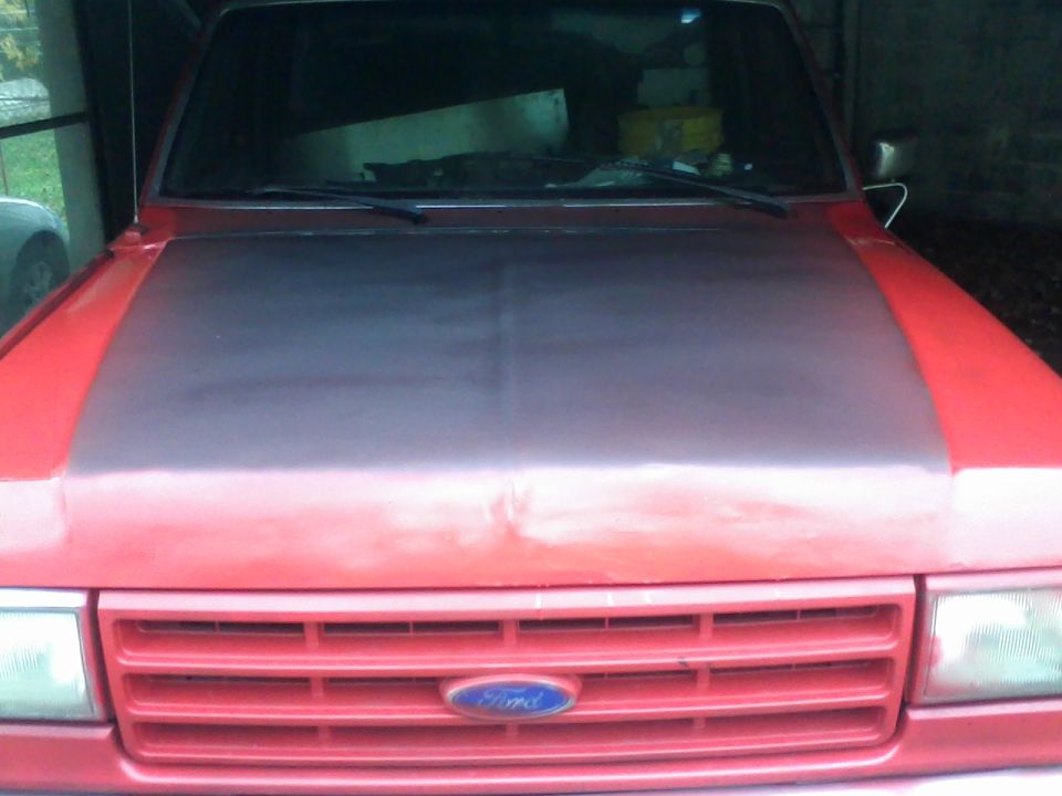Front view of a red Ford truck with a dark hood and horizontal grille. Ford logo visible