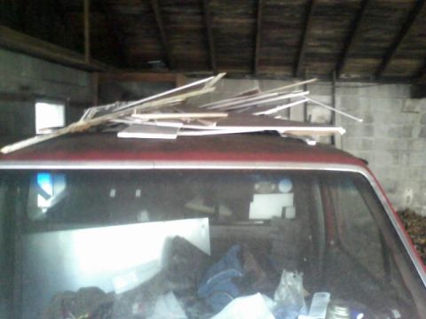 1988 Ford F-150 - The interior of the truck is filled with various items, and lumber is piled on its roof.