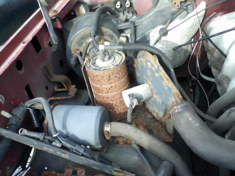 1988 Ford F-150 - Close-up view of engine bay components, including a rusty fuel filter and air filter housing.