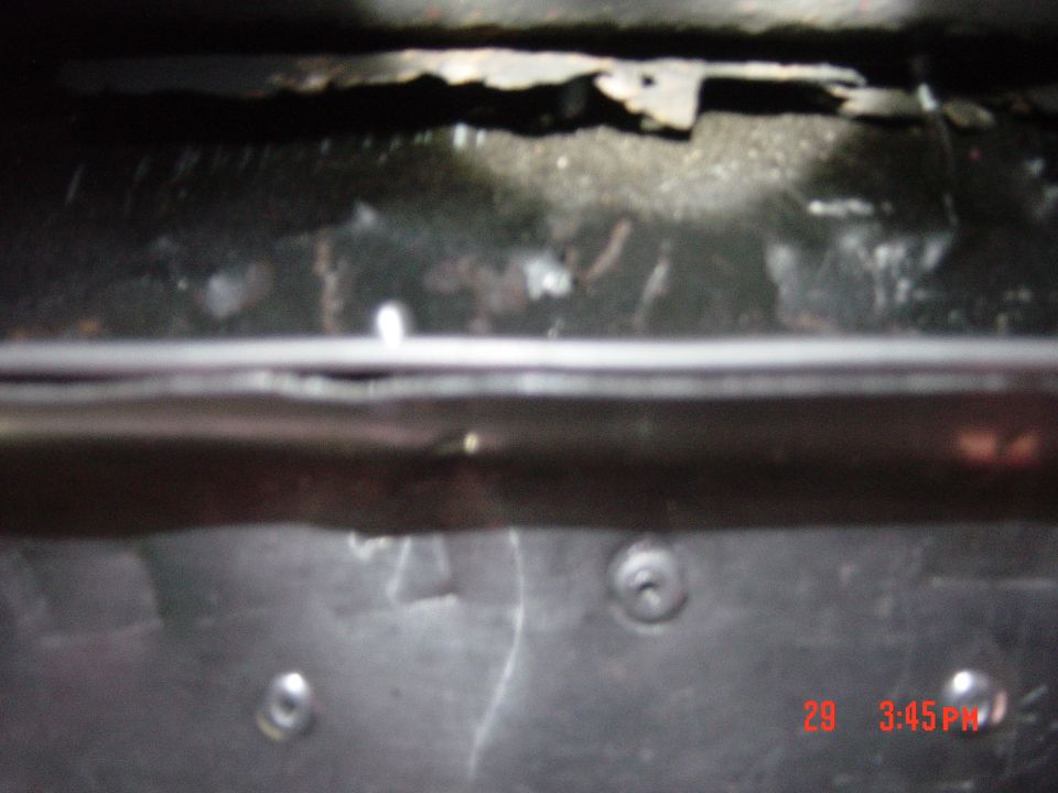 Underside of a vehicle showing rust and metal components. A timestamp and website are visible