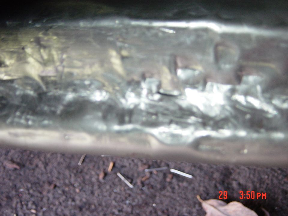 Close-up of a rusty, possibly repaired metal frame under a vehicle. Some debris is on the ground below