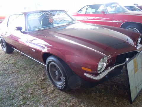 1982 Chevrolet Camaro - Maroon coupe with black hood stripe, 3/4 front view. Text visible on windshield. Another vehicle is parked behind.