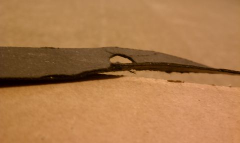 1990 Ford Bronco - A damaged automotive part is shown in a close-up view against a tan background.