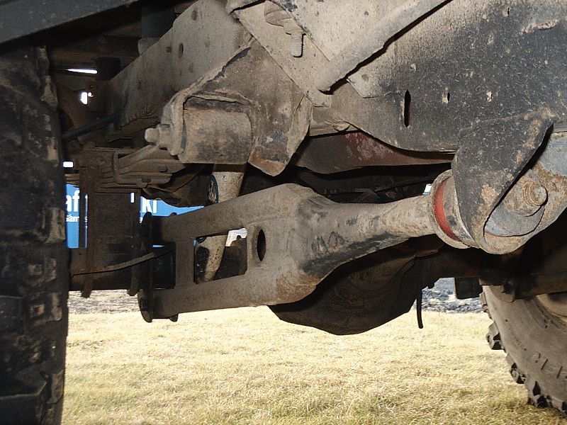 Undercarriage view of a Ford Bronco showing front axle, differential, and rusty suspension components over grass.