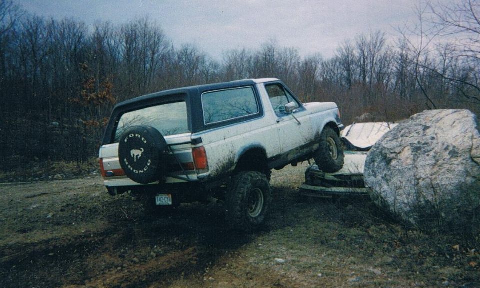 White Ford Bronco with a spare tire on the back, driving over rocks and debris
