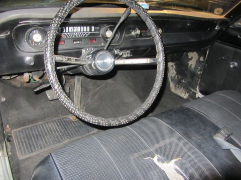 1964 Ford Ranchero - The interior of a classic car shows a worn steering wheel and cracked seat upholstery.