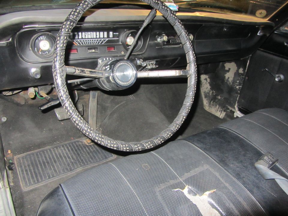 Car interior with steering wheel, dashboard, and seats. Dashboard has a speedometer and fuel gauge