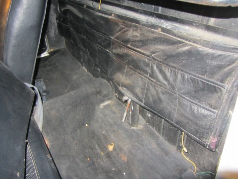 1964 Ford Ranchero - The interior of a vehicle shows a black vinyl panel with stitched pockets and dark carpeted floor.