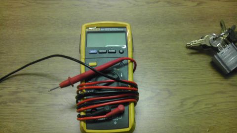 1989 Ford Bronco - A digital multimeter and a set of keys with a padlock are placed on a wooden desk.