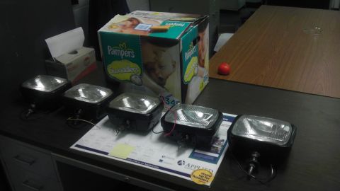 1989 Ford Bronco - A collection of four headlights are displayed on a desk, accompanied by a box of diapers and a tissue dispenser.