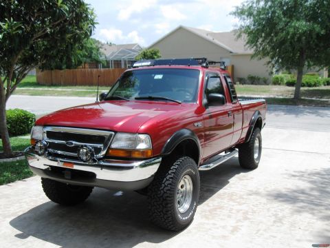 1999 Ford Ranger - This red 1999 Ford Ranger pickup truck is equipped with a roof rack and off-road tires, parked in a driveway.