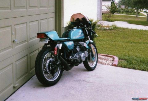 1999 Ford Ranger - A teal motorcycle is parked in front of a garage door, showing its rear profile and custom seat.