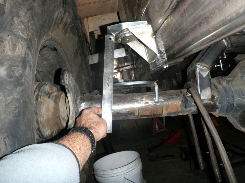 Hand holding ruler against a metal axle and custom suspension bracket