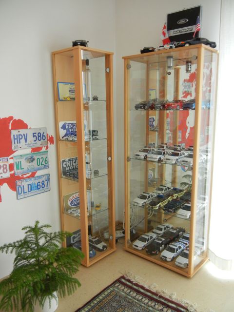 1999 Lincoln Town Car - A collection of model cars is neatly arranged in two tall glass display cabinets, with various license plates adorning the wall behind them.
