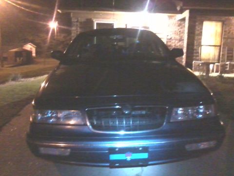 1997 Mercury Grand Marquis - The front of a dark-colored sedan is visible, parked outside a house at night.
