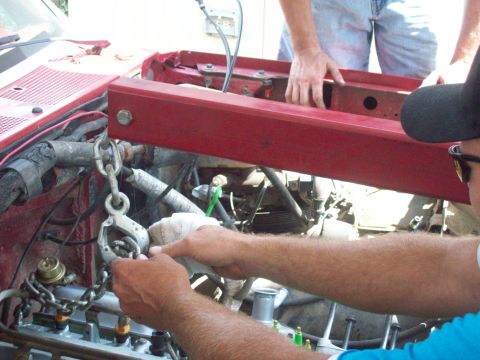 1989 Ford Bronco - Mechanics use an engine hoist and chains to remove the engine from a red vehicle.