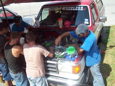 1989 Ford Bronco - Several individuals are gathered around the open hood of a 1989 Ford Bronco, appearing to work on the engine. A "Weekend 4-Wheelers" sticke…