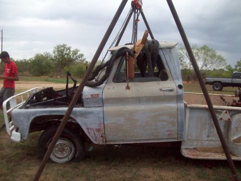 1989 Ford Bronco - A light blue pickup truck, possibly a Chevrolet, is suspended by a crane. Another pickup truck is visible in the background.