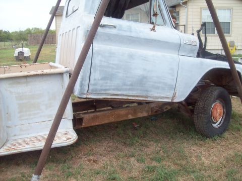 1989 Ford Bronco - This old pickup truck body is undergoing restoration work outdoors, supported by metal poles.