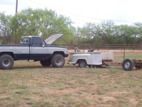 1989 Ford Bronco - Lifted pickup truck towing a trailer with a truck bed. The trailer is a chassis with a bed and spare tire.
