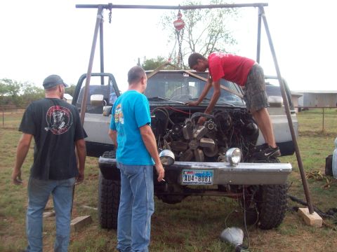 1989 Ford Bronco - Three men work on a truck that has had its engine removed, with a hoist overhead.