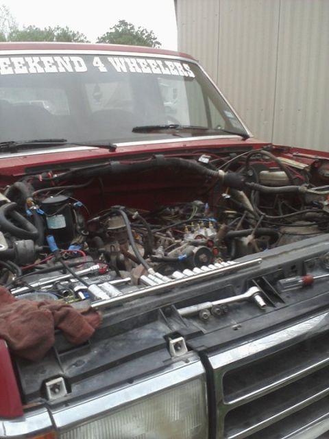 1989 Ford Bronco - A red Ford truck's engine bay is exposed, with tools laid out on the grille.