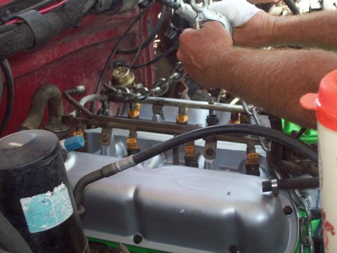 1989 Ford Bronco - Hands work on the fuel injection system within the engine bay.
