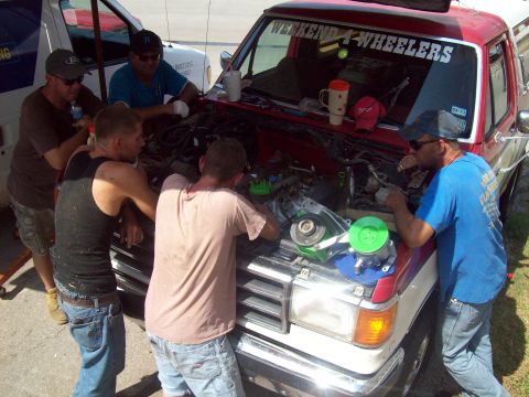 1989 Ford Bronco - Mechanics work on a pickup truck's engine bay, with another vehicle visible in the background.