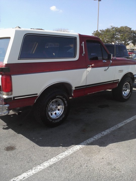 Red and white Ford Bronco parked in a lot. Side view