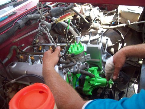 1989 Ford Bronco - Mechanics work on an engine, with a chain hoist supporting the assembly and various hoses and parts visible.