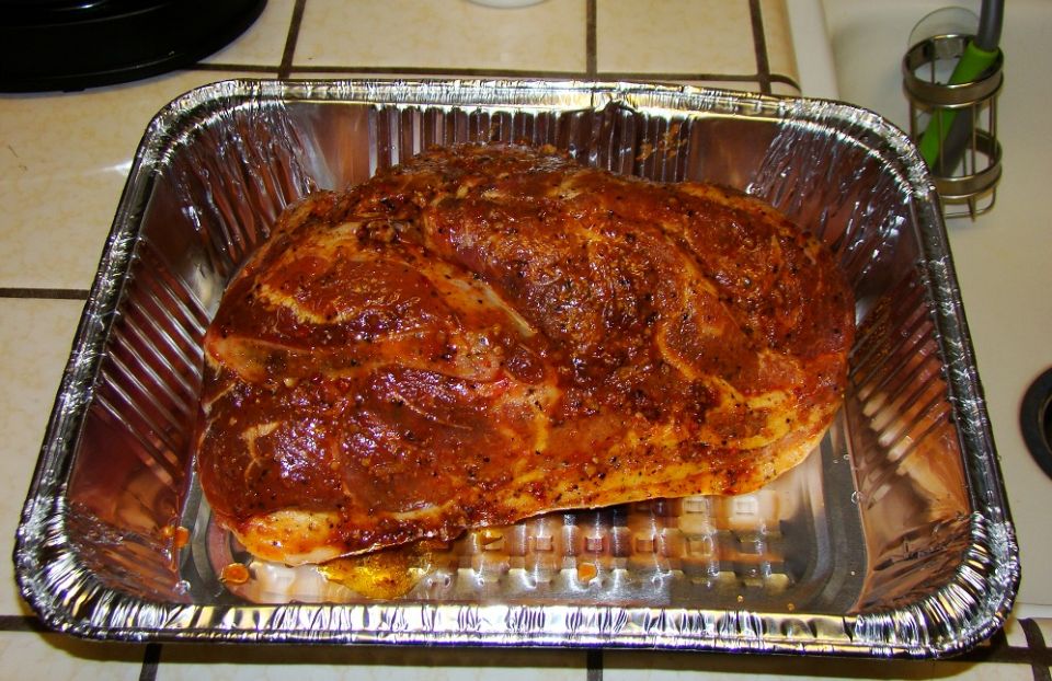 Raw pork shoulder seasoned and in a disposable foil pan