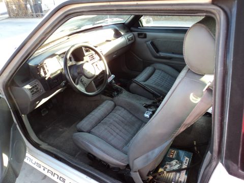 1989 Ford Mustang - The interior of a 1989 Ford Mustang is visible from the side, revealing the dashboard and seats.