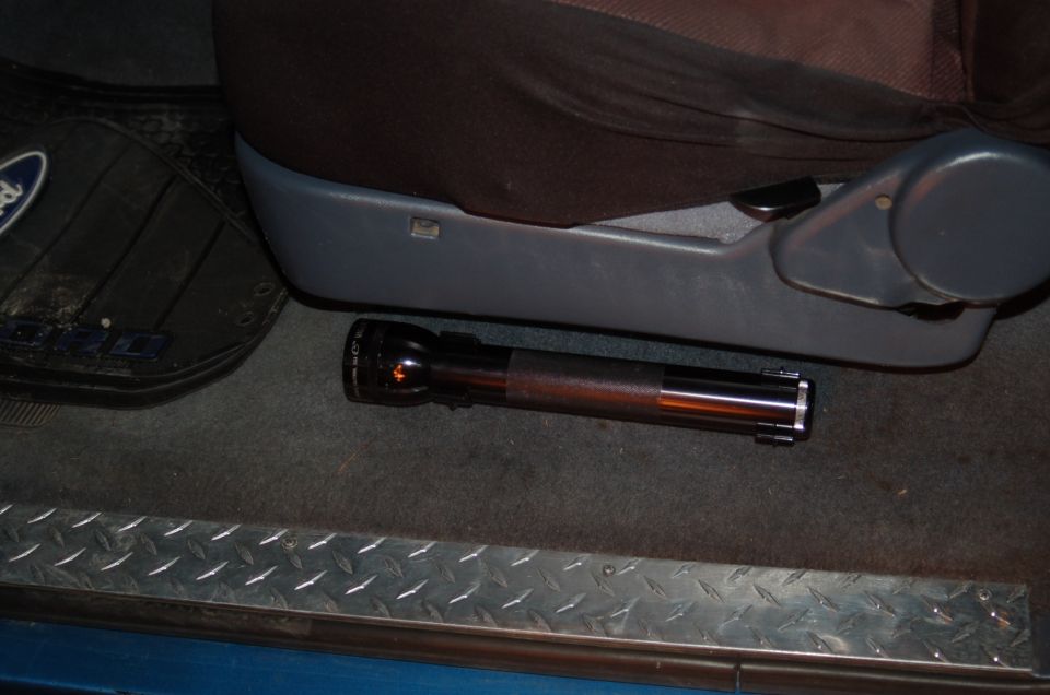 Black flashlight lying on a Ford floor mat next to a vehicle seat